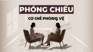 Hình ảnh hai người phụ nữ ngồi đối diện nhau trên ghế, phía trên có chữ 'PHÓNG CHIẾU' và 'CƠ CHẾ PHÒNG VỆ', minh họa khái niệm phóng chiếu như một cơ chế bảo vệ tâm lý.